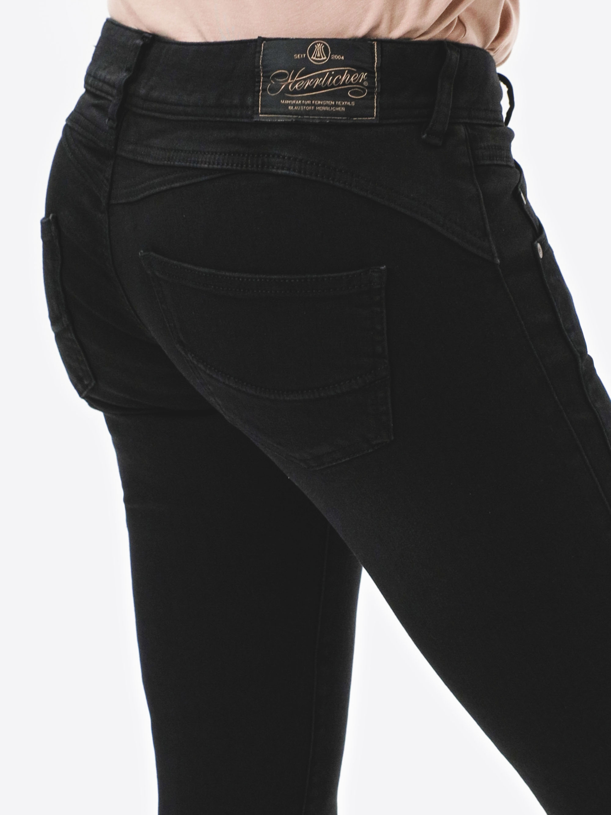 Eine Person, die eine schwarze Jeans trägt, von hinten gesehen, wobei der Taschen- und Bundbereich mit einem sichtbaren Markenetikett über der rechten Tasche zu sehen ist.