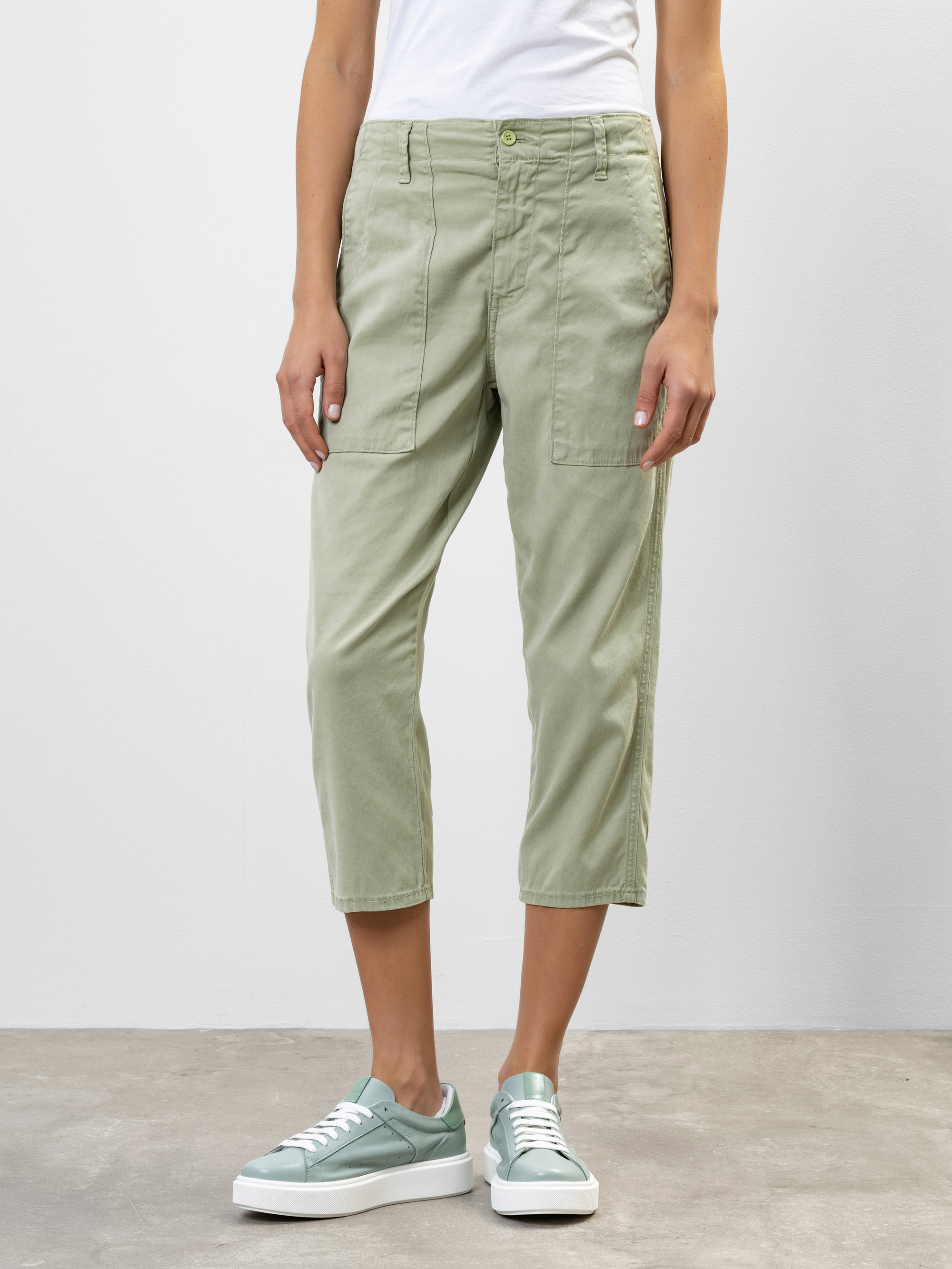 Eine Person, die eine hellgrüne kurze Cargohose und mintgrüne Turnschuhe trägt, steht vor einem schlichten weißen Hintergrund und hat die Arme entspannt an der Seite.