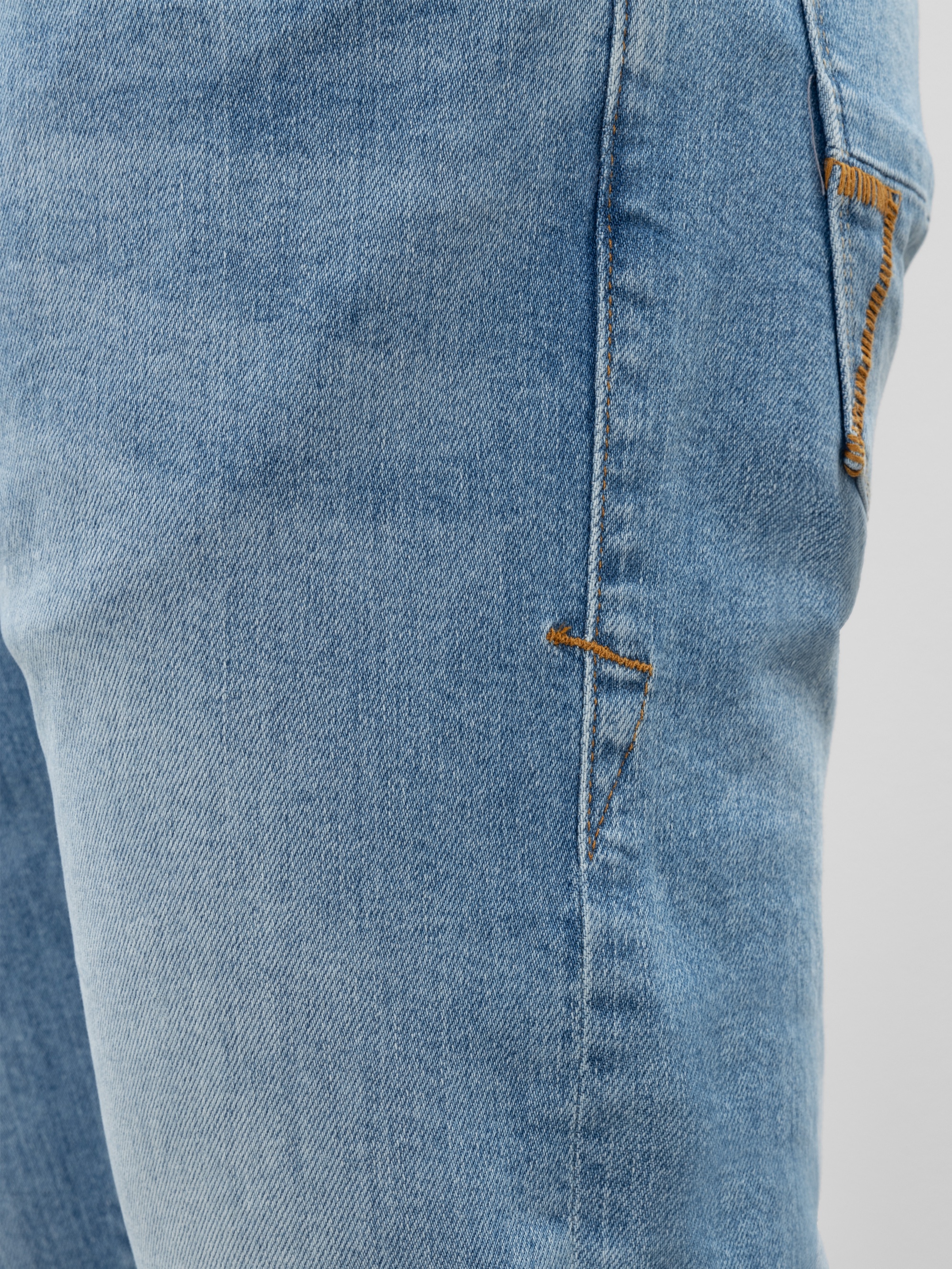 Nahaufnahme einer hellblauen Denim-Jeans mit einer Seitentasche mit orangefarbenen Ziernähten.