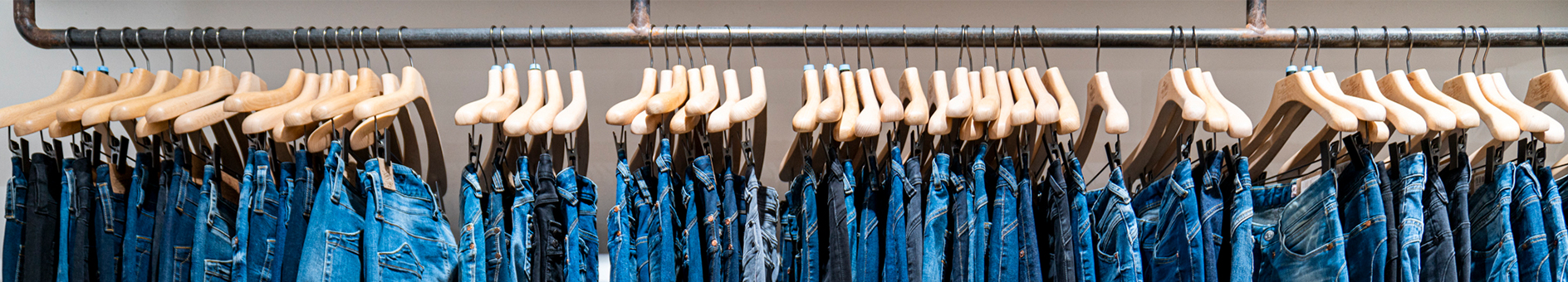 Eine Reihe blauer Jeans, die auf Holzbügeln an einem metallenen Kleiderständer hängen und in einem Geschäft ordentlich ausgestellt sind.