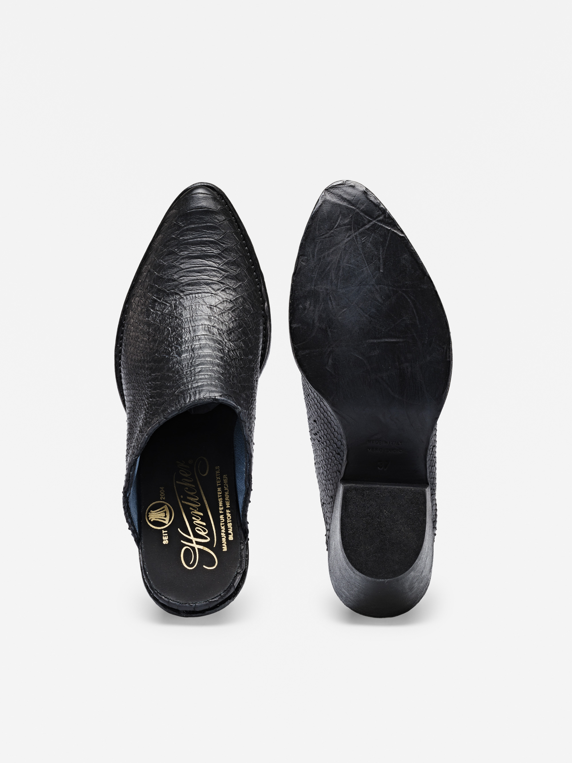 Ein Paar schwarze Slipper, einer mit strukturiertem Oberleder und goldener Innensohle, der andere mit glatter, leicht abgenutzter Ledersohle und schwarzem Absatz.