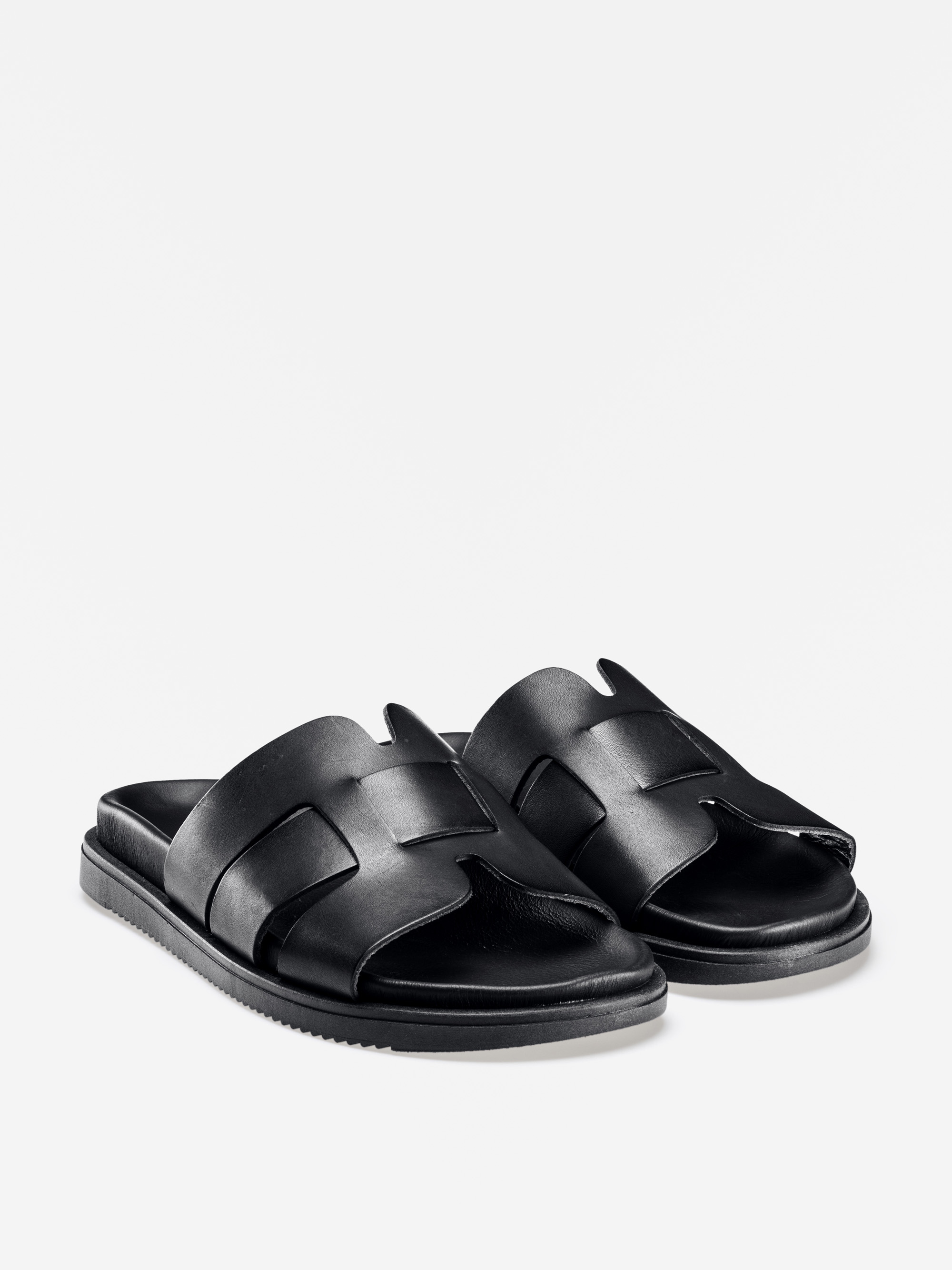 Ein Paar schwarzer Ledersandalen mit breiten, ineinandergreifenden Riemen und flachen Sohlen, die auf einem schlichten weißen Hintergrund abgebildet sind.