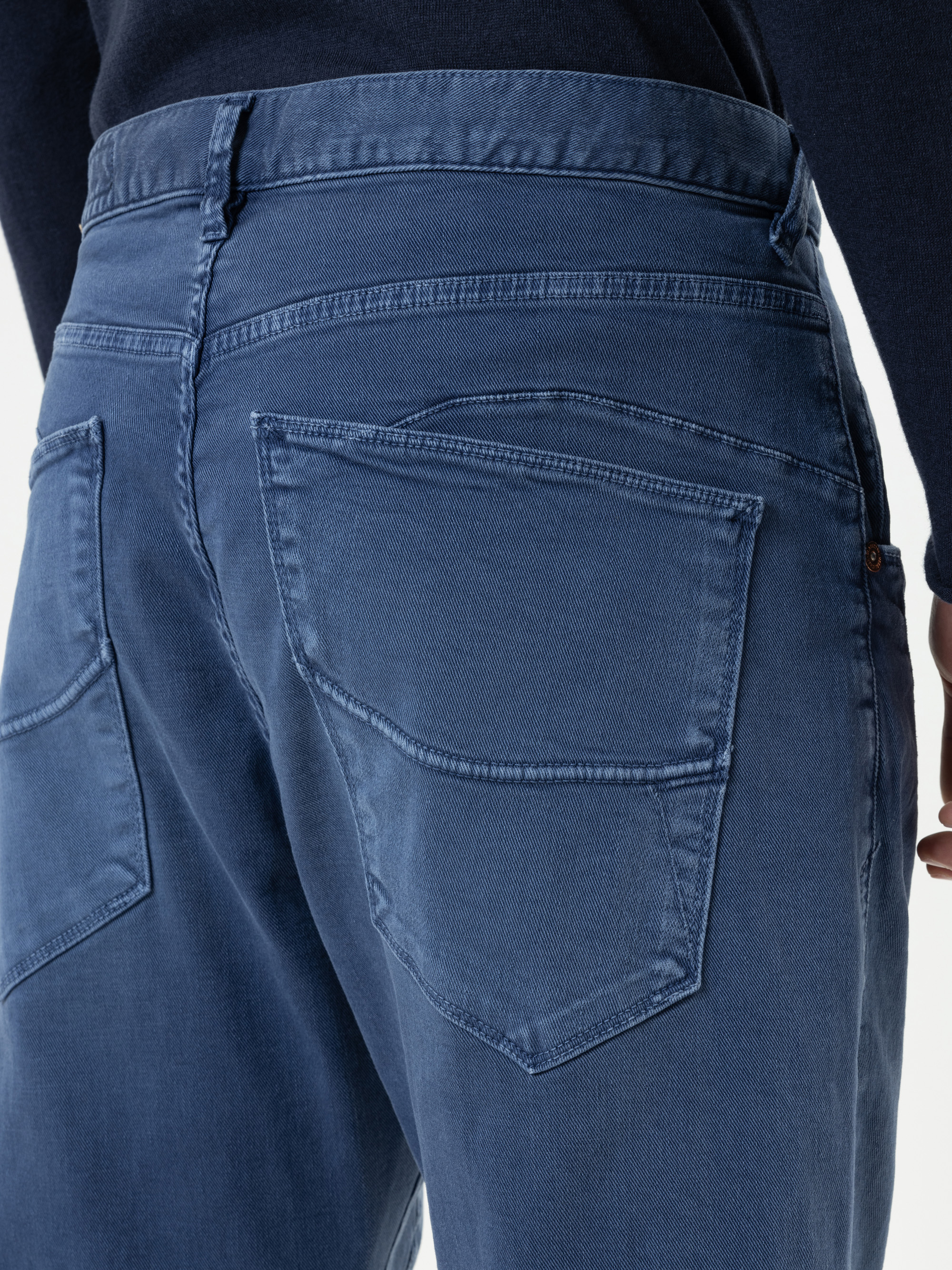 Nahaufnahme des Rückens einer Person, die eine blaue Jeans und ein dunkles langärmeliges Oberteil trägt, wobei die Gesäßtaschen und Details der Jeansnähte zu sehen sind.