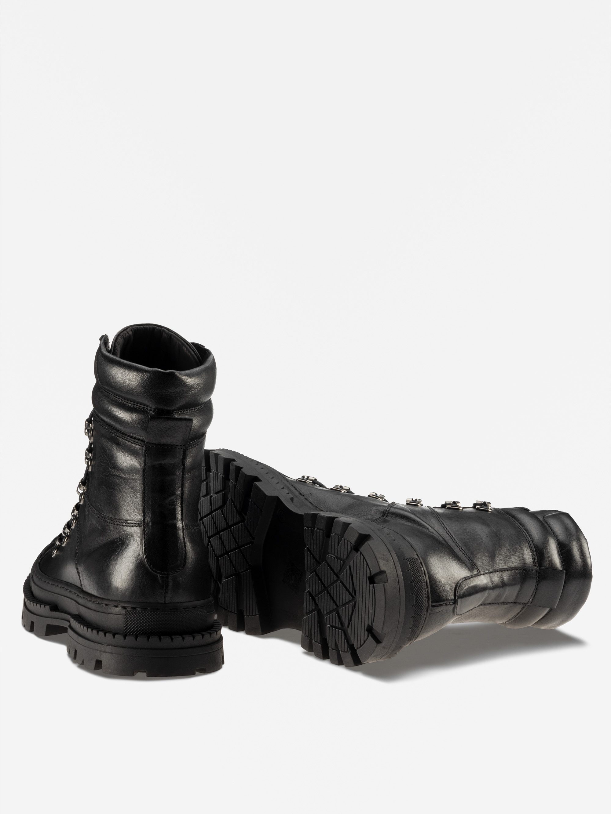Ein Paar schwarze Lederschnürstiefel mit dicken, robusten Gummisohlen; ein Stiefel steht aufrecht und zeigt die Rückseite, während der andere auf der Seite liegt und das Profil zeigt.