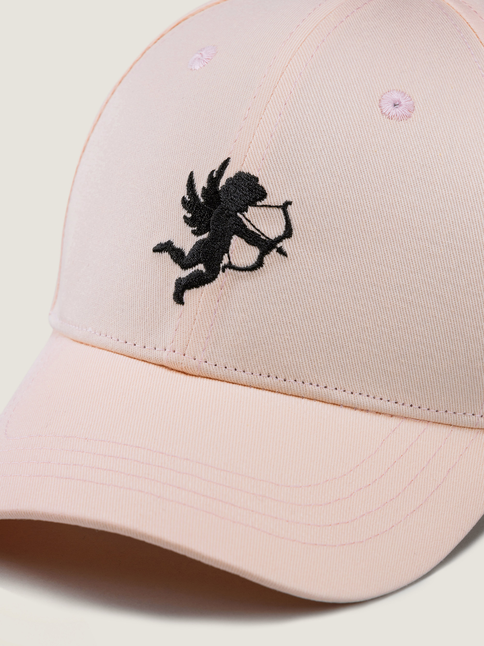 Eine hellrosa Baseballmütze mit einer aufgestickten schwarzen Silhouette eines geflügelten Amors, der einen Pfeil und Bogen hält, auf der Vorderseite.