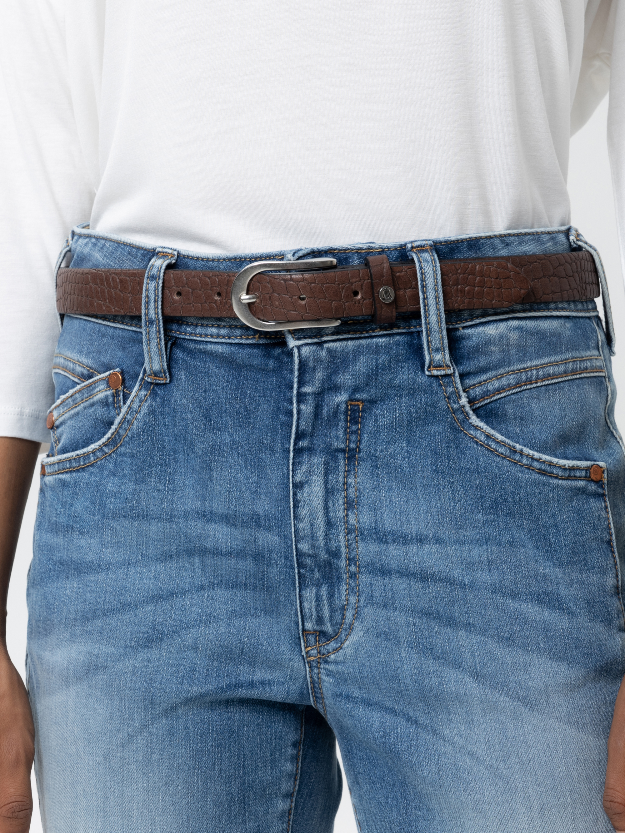 Eine Person, die ein weißes Hemd trägt, das in eine blaue Jeans mit einem braunen, strukturierten Ledergürtel gesteckt ist, der von der Taille bis zur Mitte des Oberschenkels reicht.