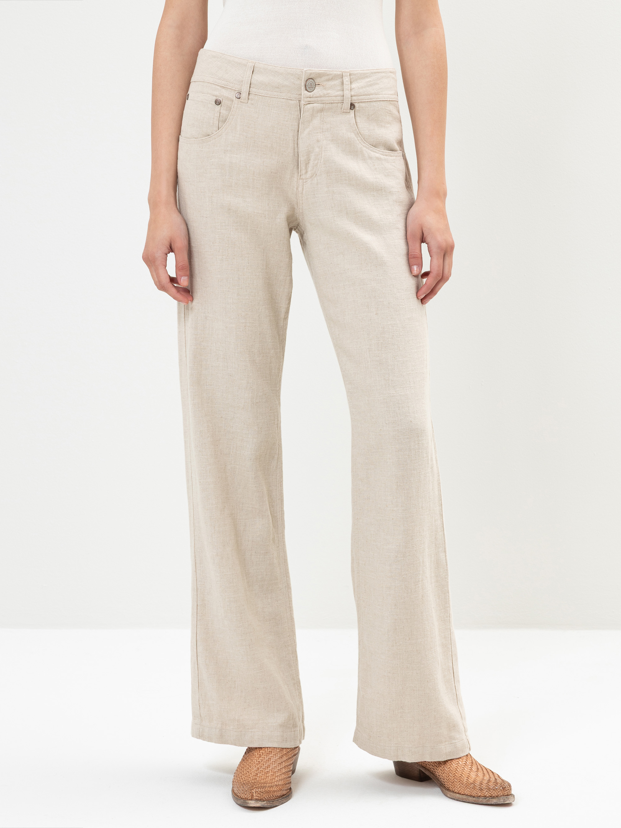 Eine Person in hellbeiger, weit geschnittener Hose und hellbraunen Webschuhen steht vor einem schlichten weißen Hintergrund. Nur der untere Teil des Oberkörpers und die Beine sind sichtbar.