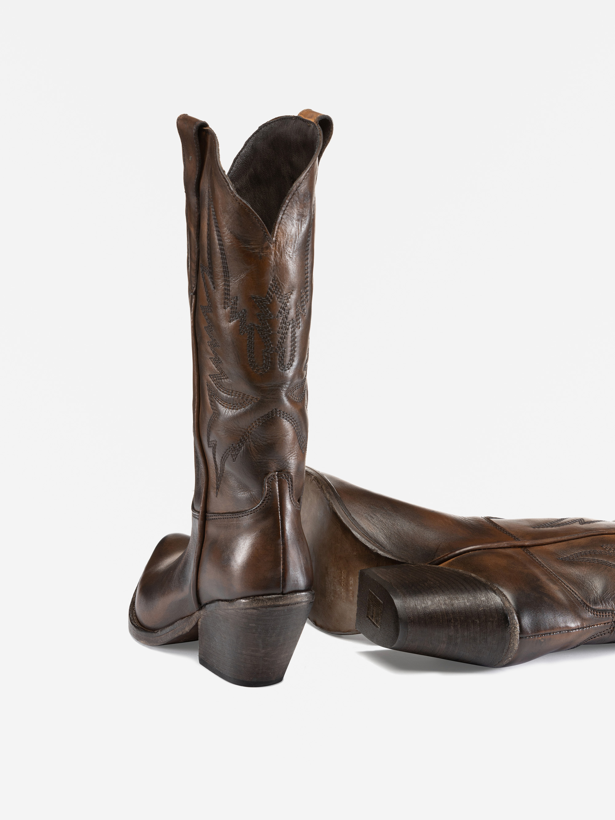 Ein Paar Cowboystiefel aus braunem Leder mit Ziernähten; ein Stiefel steht aufrecht, während der andere auf der Seite liegt und die Sohle und den Absatz zeigt.