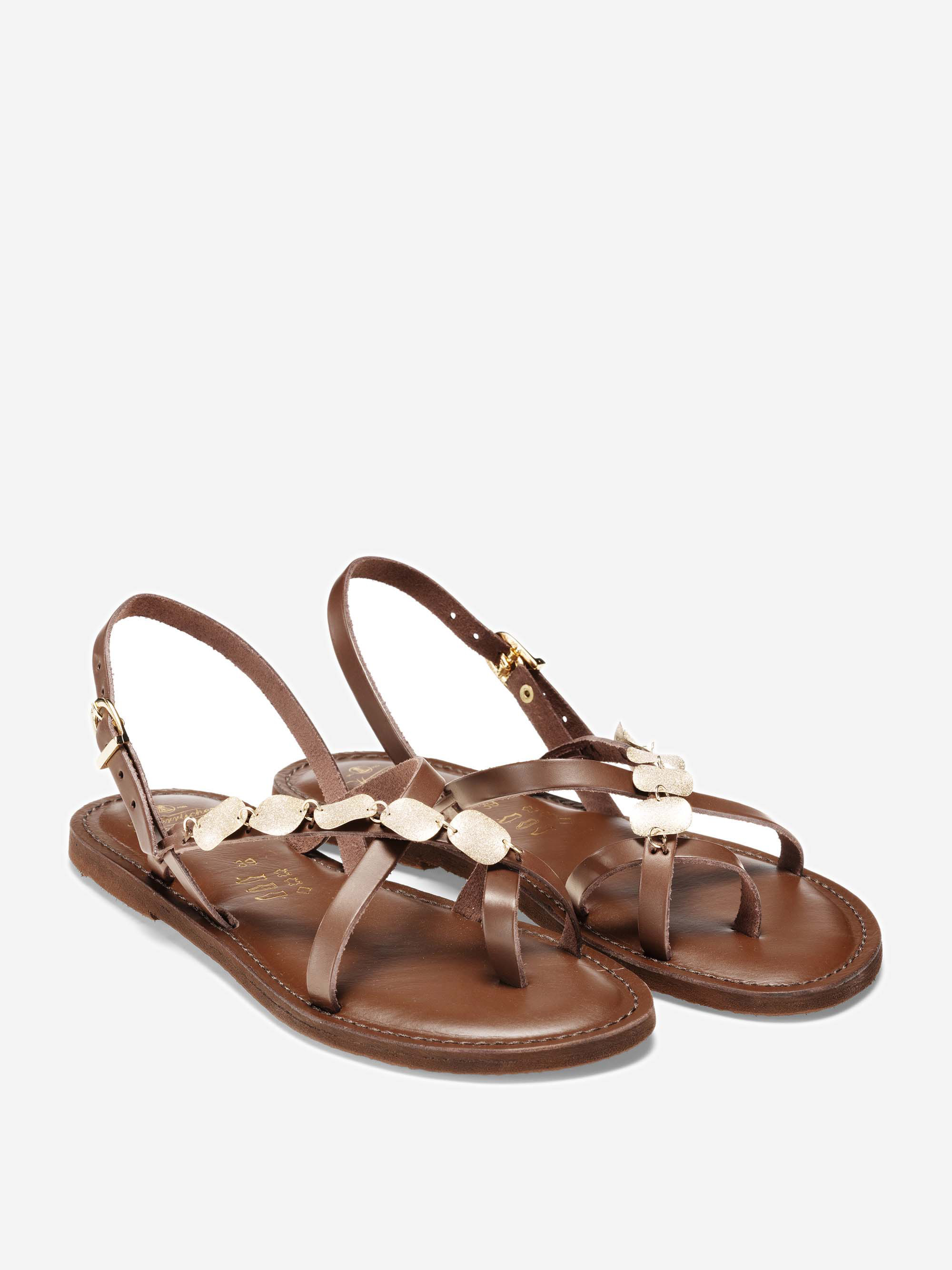 Ein Paar braune flache Ledersandalen mit Knöchelriemen und goldenen Schnallenverschlüssen. Die Sandalen verfügen über dekorative Blattgold-Akzente entlang der oberen Riemen. Sie sind auf einem schlichten weißen Hintergrund dargestellt.