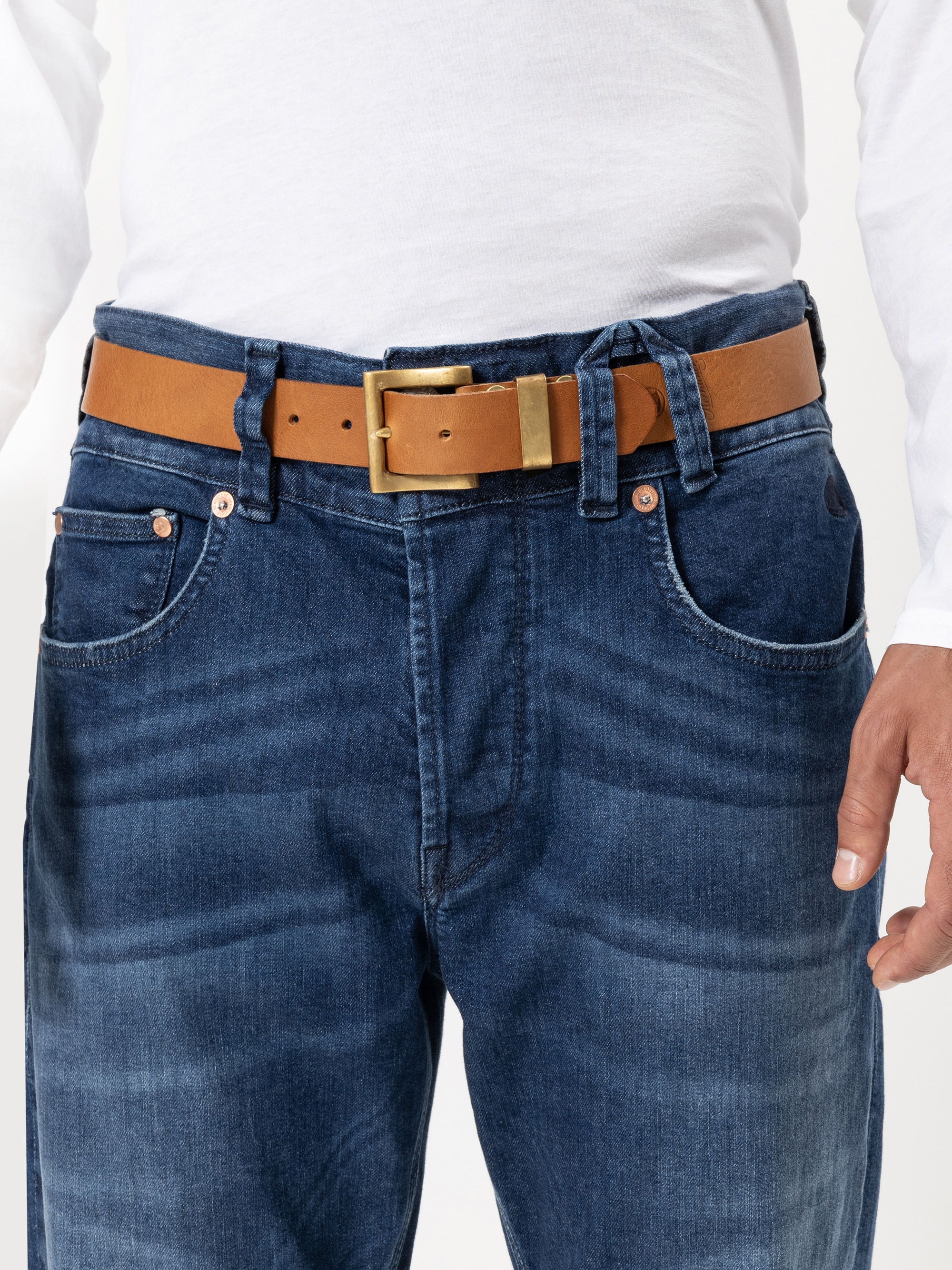 Eine Person, die eine blaue Jeans und einen braunen Ledergürtel mit einer goldenen Schnalle trägt, bekleidet mit einem weißen langärmeligen Hemd. Nur der untere Teil des Oberkörpers und die Hände sind sichtbar.