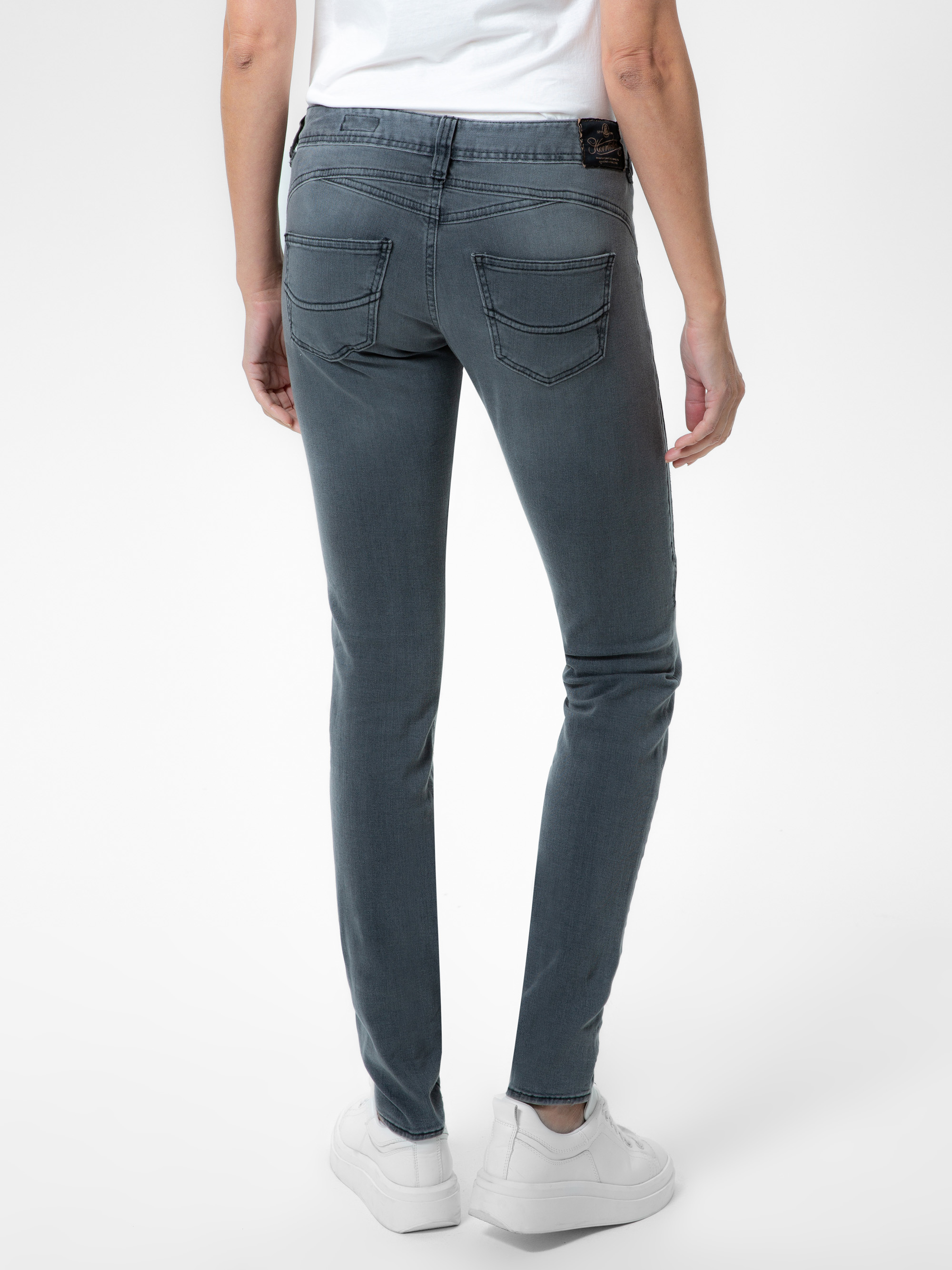 Eine Person steht mit dem Gesicht nach unten, trägt ein weißes T-Shirt, eine graue Jeans mit sichtbaren Gesäßtaschen und weiße Turnschuhe vor einem schlichten weißen Hintergrund.