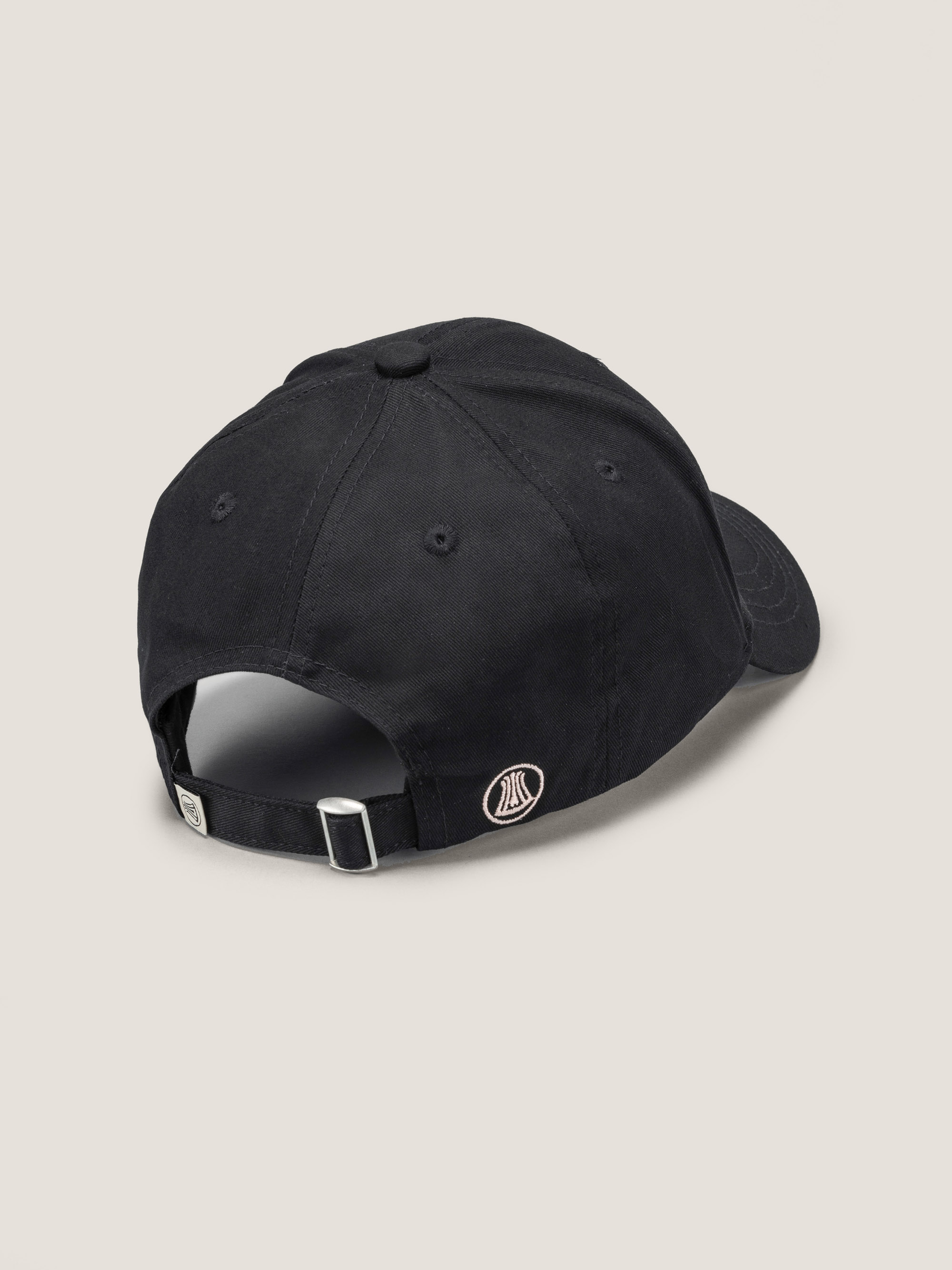 Schwarze Baseballkappe, von hinten gesehen, mit einem verstellbaren Riemen mit Metallschnalle und einem kleinen kreisförmigen gestickten Aufnäher in der Nähe der Öffnung.