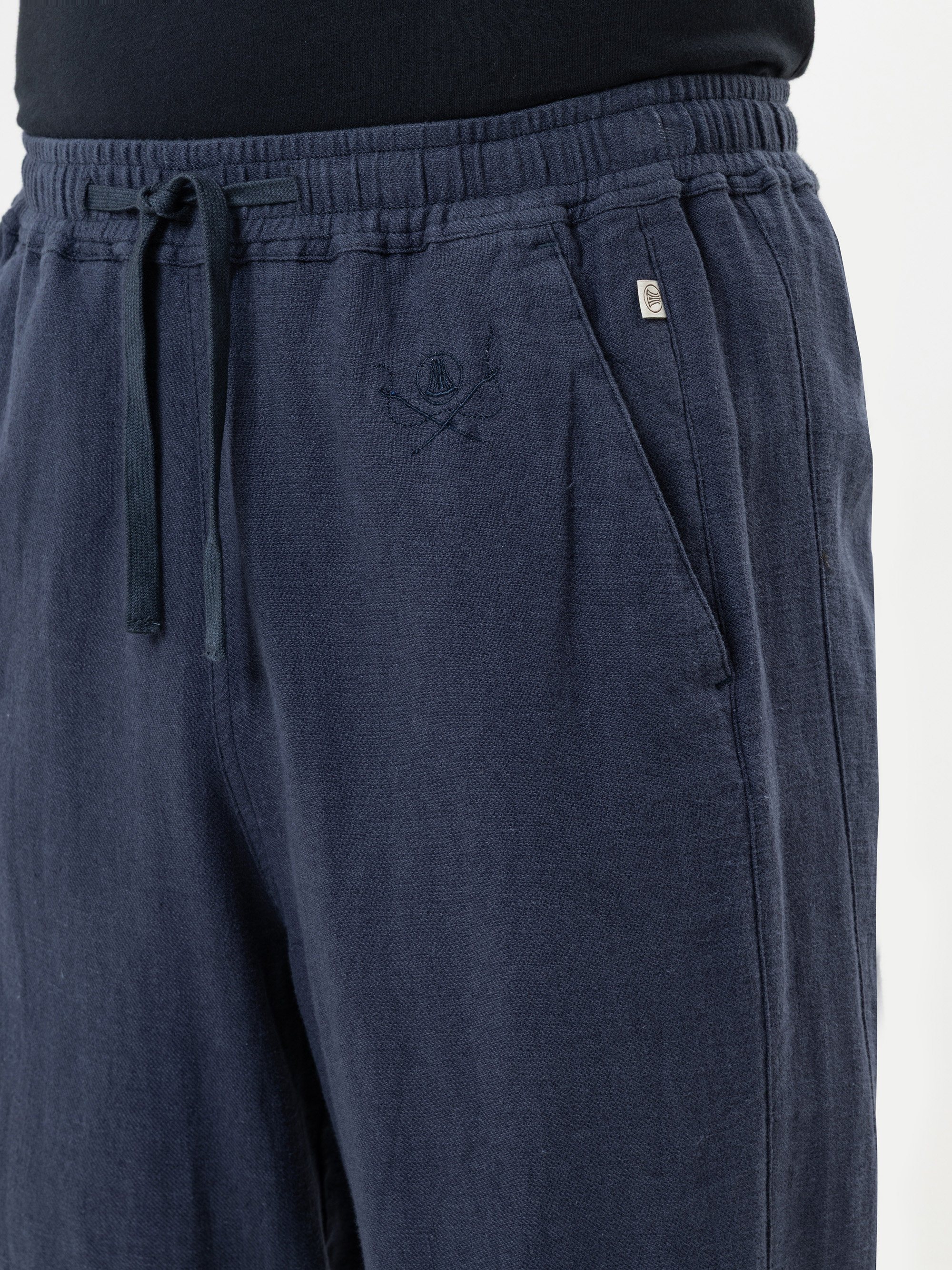 Nahaufnahme einer Person, die eine dunkelblaue Jogginghose mit Kordelzug, Stickereien und Seitentaschen trägt, kombiniert mit einem schwarzen Oberteil.