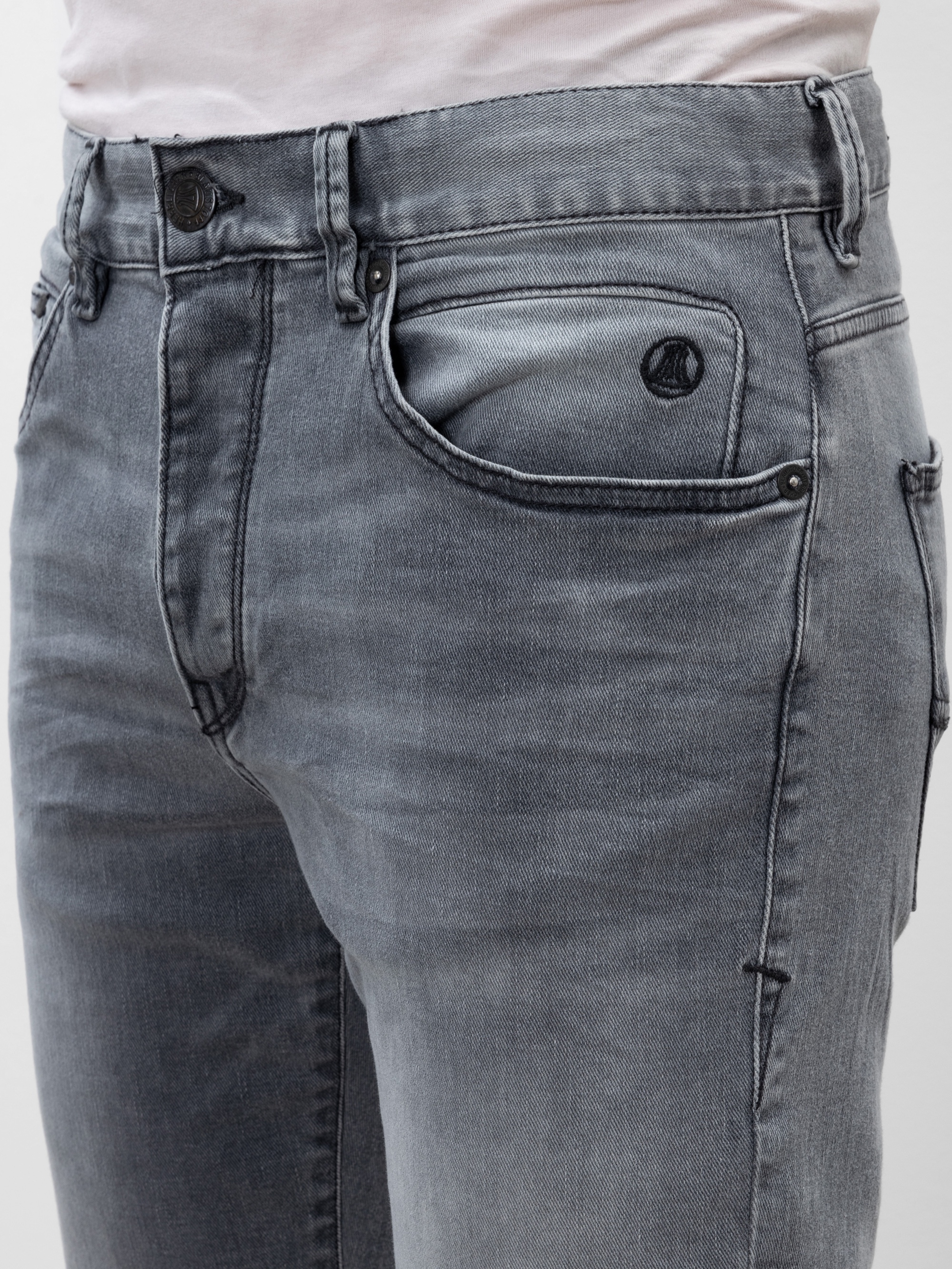 Nahaufnahme einer Person, die eine hellgraue Jeans mit Knopf und Reißverschluss, Gürtelschlaufen und Vordertaschen trägt. Der Bund und der obere Teil der Jeans sind sichtbar. Dazu trägt sie ein helles Hemd.
