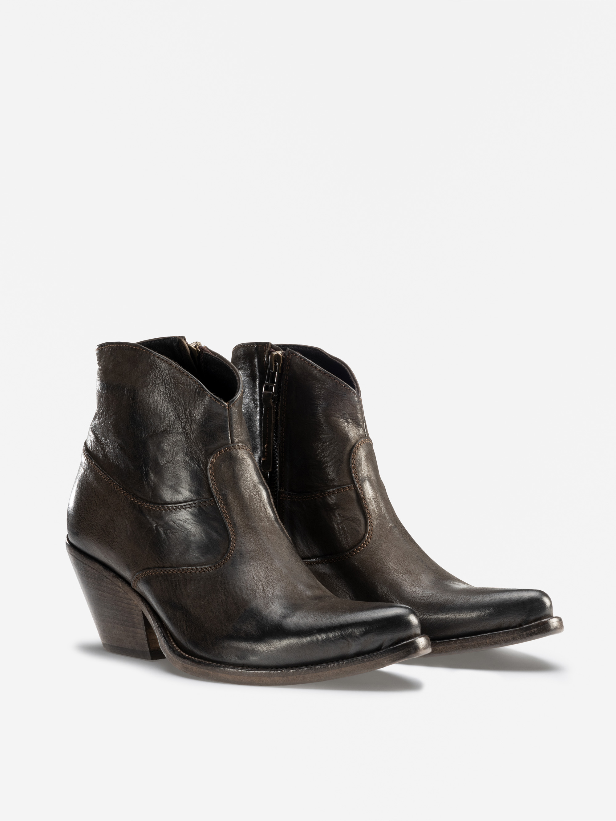 Ein Paar schwarze Lederstiefel mit leicht spitzer Spitze, seitlichen Reißverschlüssen und gestapelten Absätzen. Die Stiefel haben eine abgenutzte, notleidende Oberfläche und sichtbare Nähte Details.