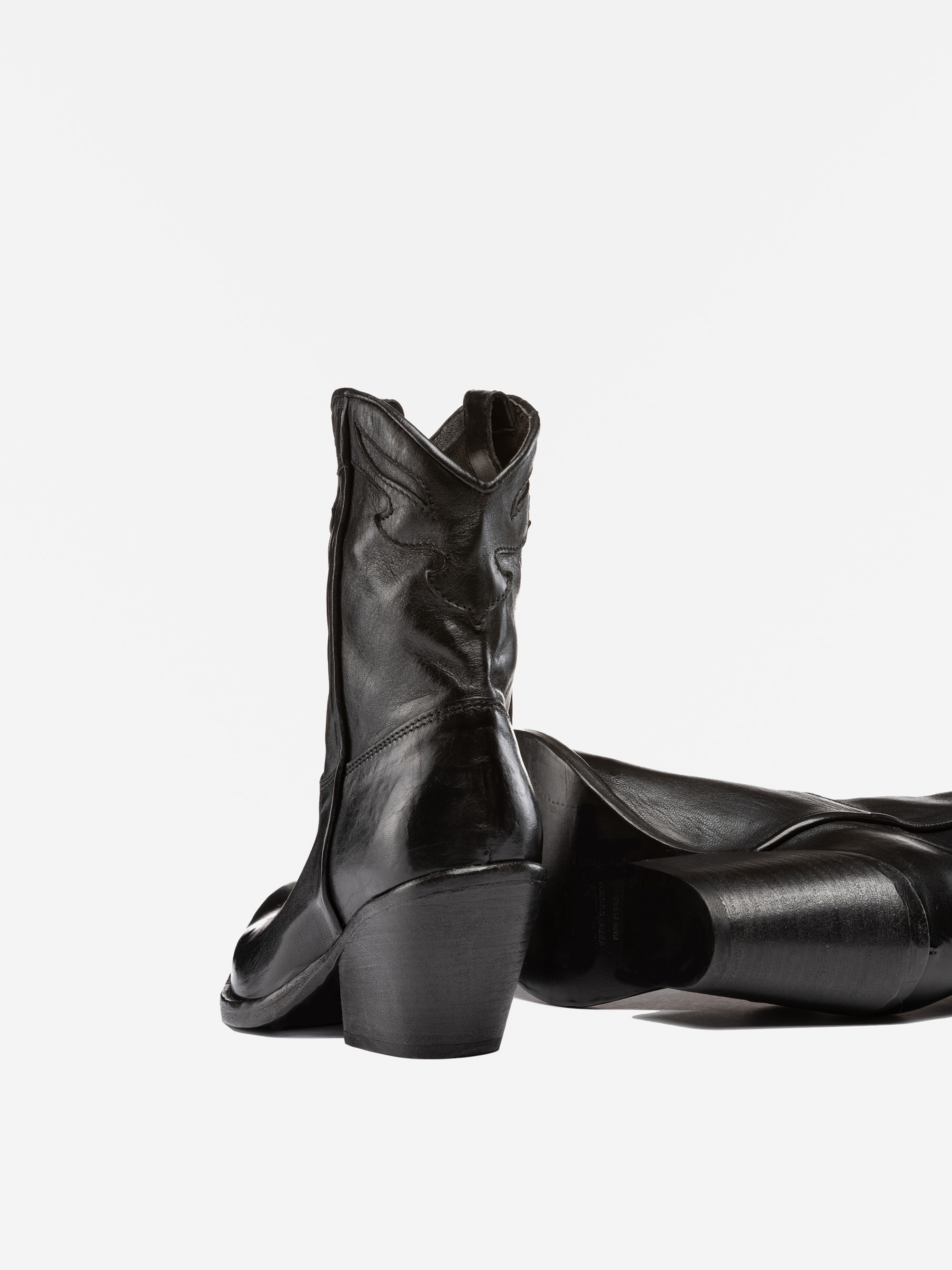 Zwei schwarze Cowboystiefel aus Leder, einer aufrecht stehend, der andere auf der Seite liegend, auf weißem Hintergrund.