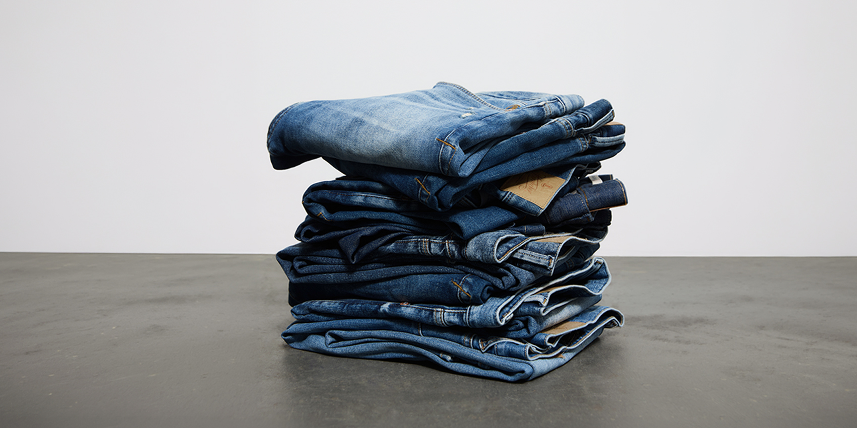 Ein ordentlich gefalteter Stapel Bluejeans liegt auf einer grauen Fläche vor einem schlichten weißen Hintergrund.
