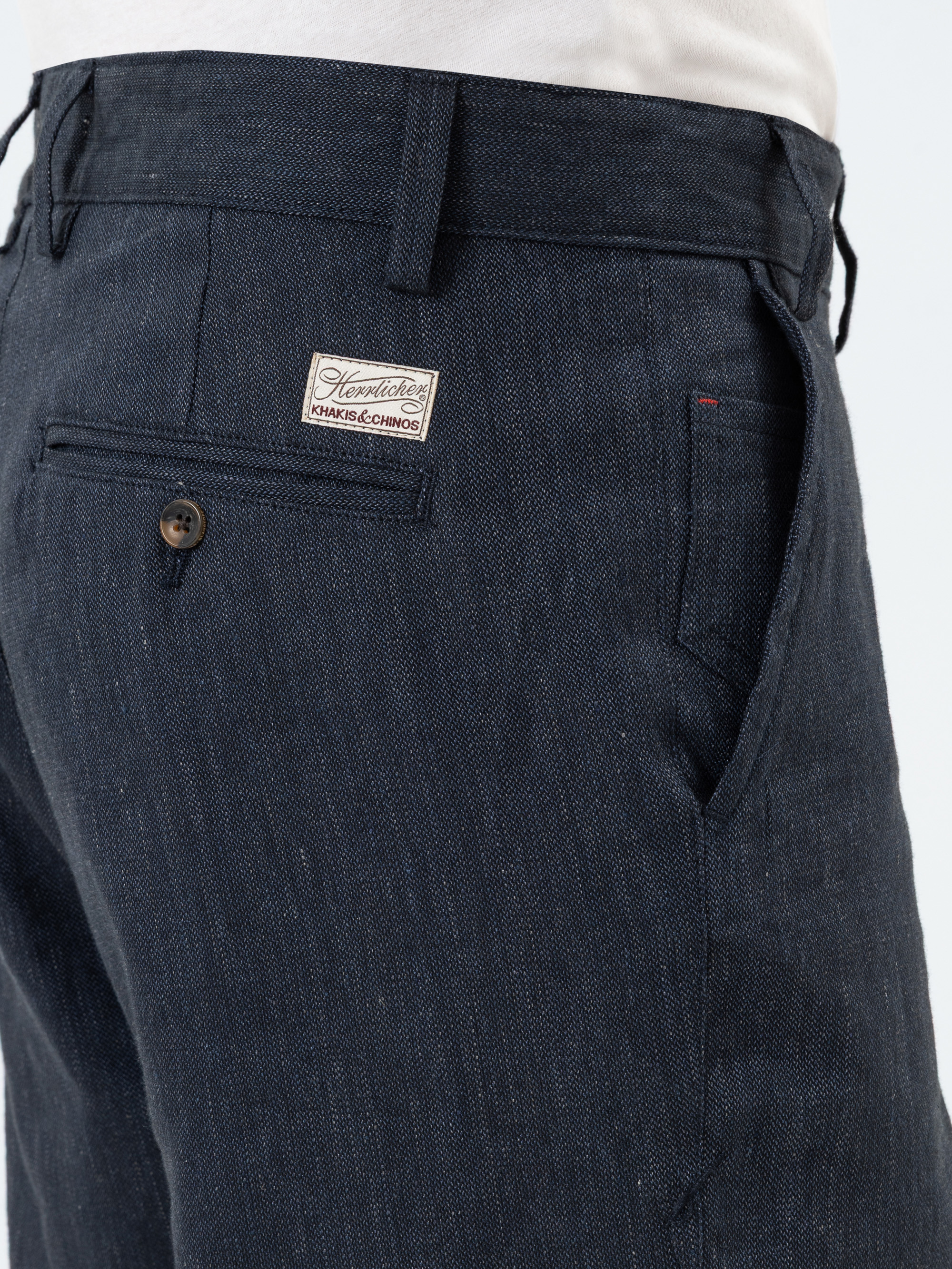 Nahaufnahme einer Person, die eine dunkle Jeanshose und ein weißes Hemd trägt. Die Hose hat ein Etikett über der Gesäßtasche und eine geknöpfte Gesäßtasche auf der rechten Seite. Der Stoff hat eine feine Textur.