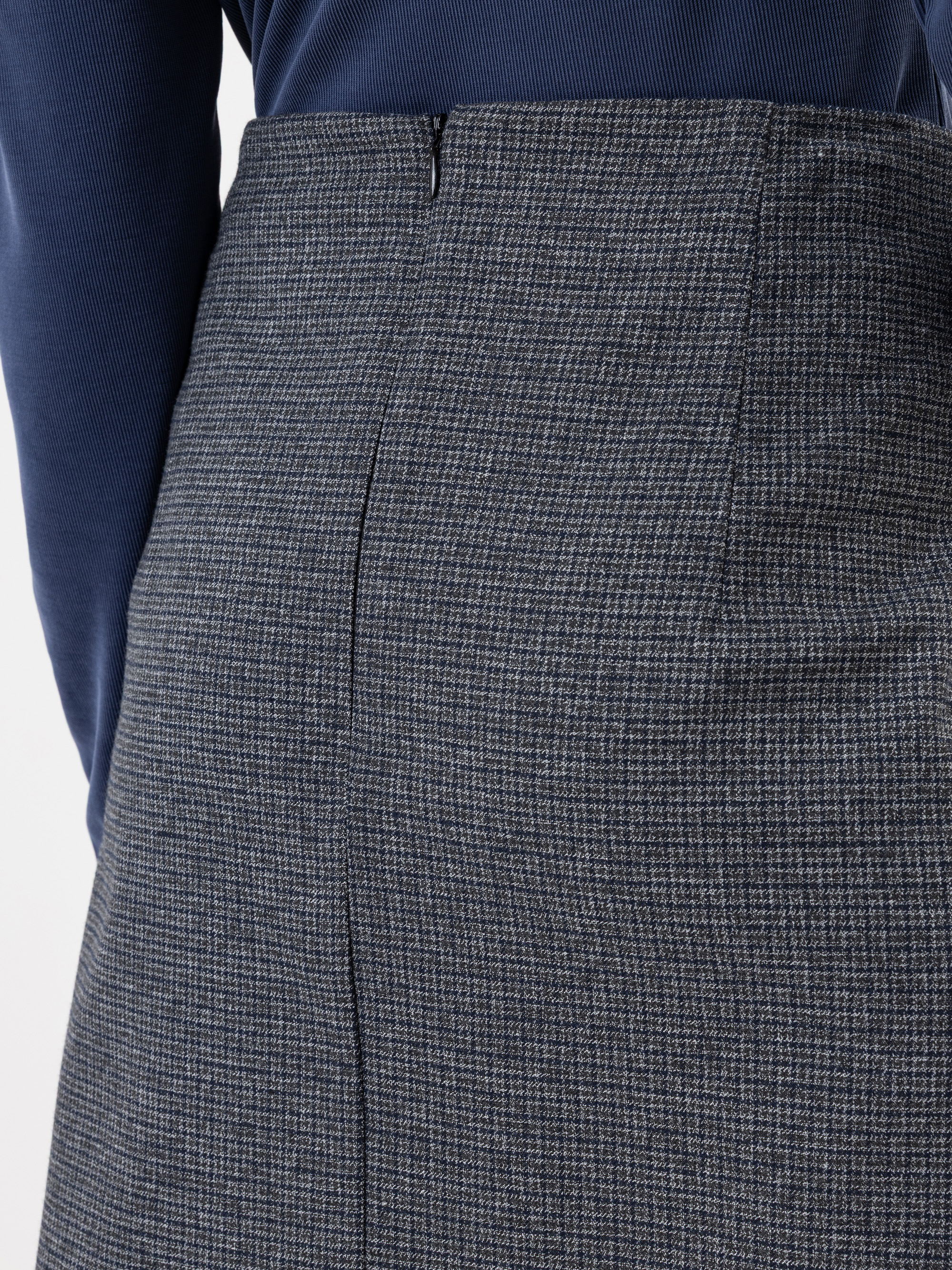 Nahaufnahme einer Person, die ein marineblaues, geripptes, langärmeliges Hemd trägt, das in einen hochtaillierten, grau karierten Rock gesteckt ist, von hinten gesehen.