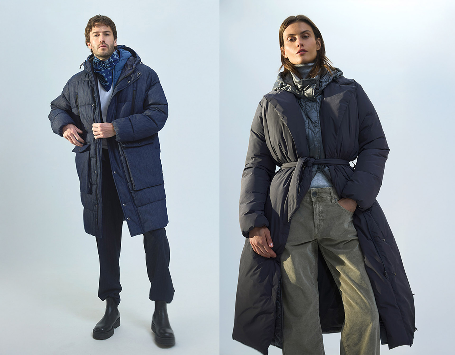 Zwei Modelle tragen lange, dunkle Puffermäntel mit Kapuzen. Das Modell auf der linken Seite trägt eine schwarze Hose und Stiefel, das Modell auf der rechten Seite einen Mantel mit Gürtel, eine Hose mit weitem Bein und ein Halstuch. Beide posieren vor e