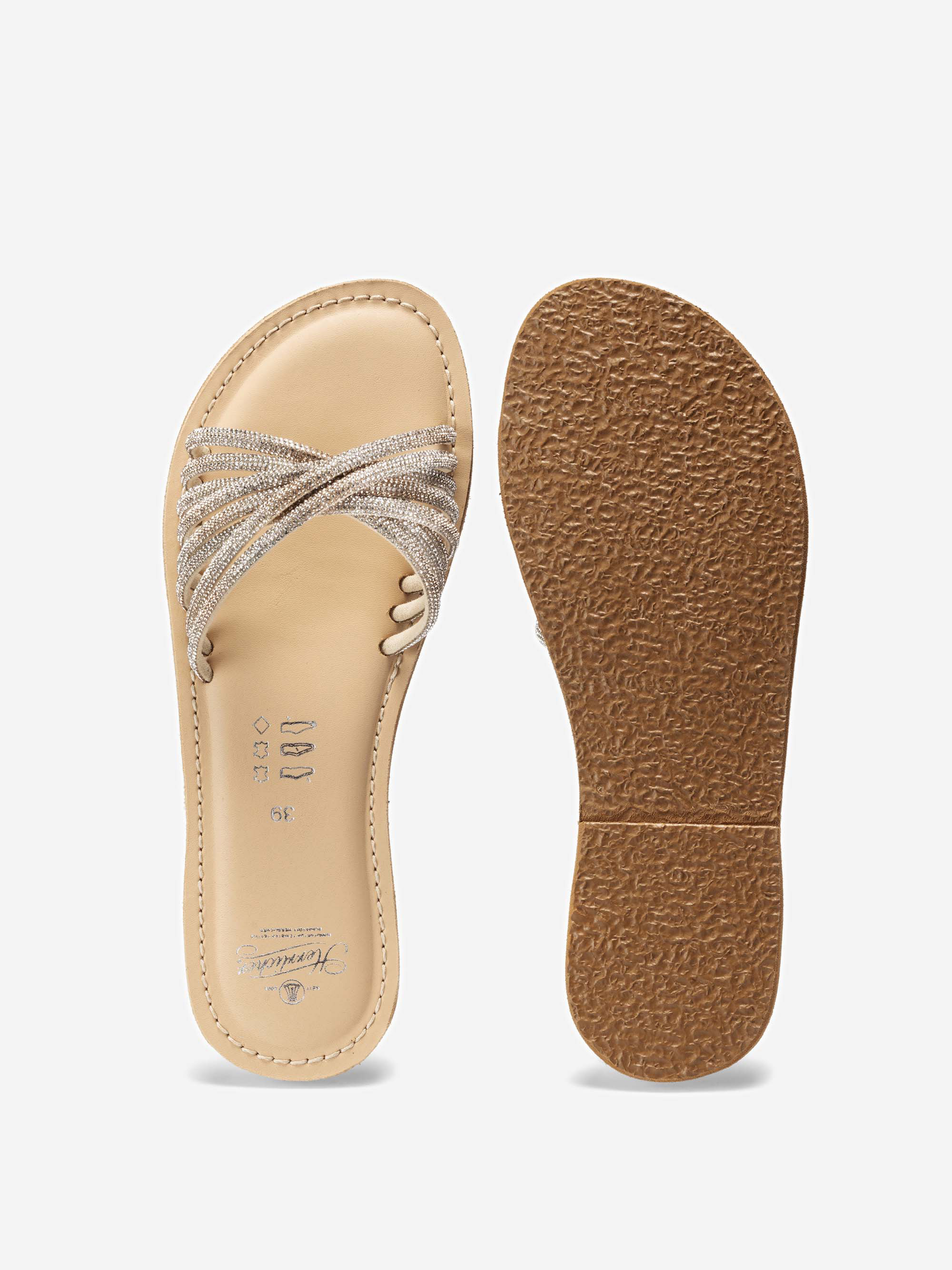 Ein Paar beigefarbene flache Sandalen mit strukturierten Gummisohlen; eine Sandale zeigt das Oberteil mit überkreuzten, glitzernden Riemen, die andere die untere Sohle.